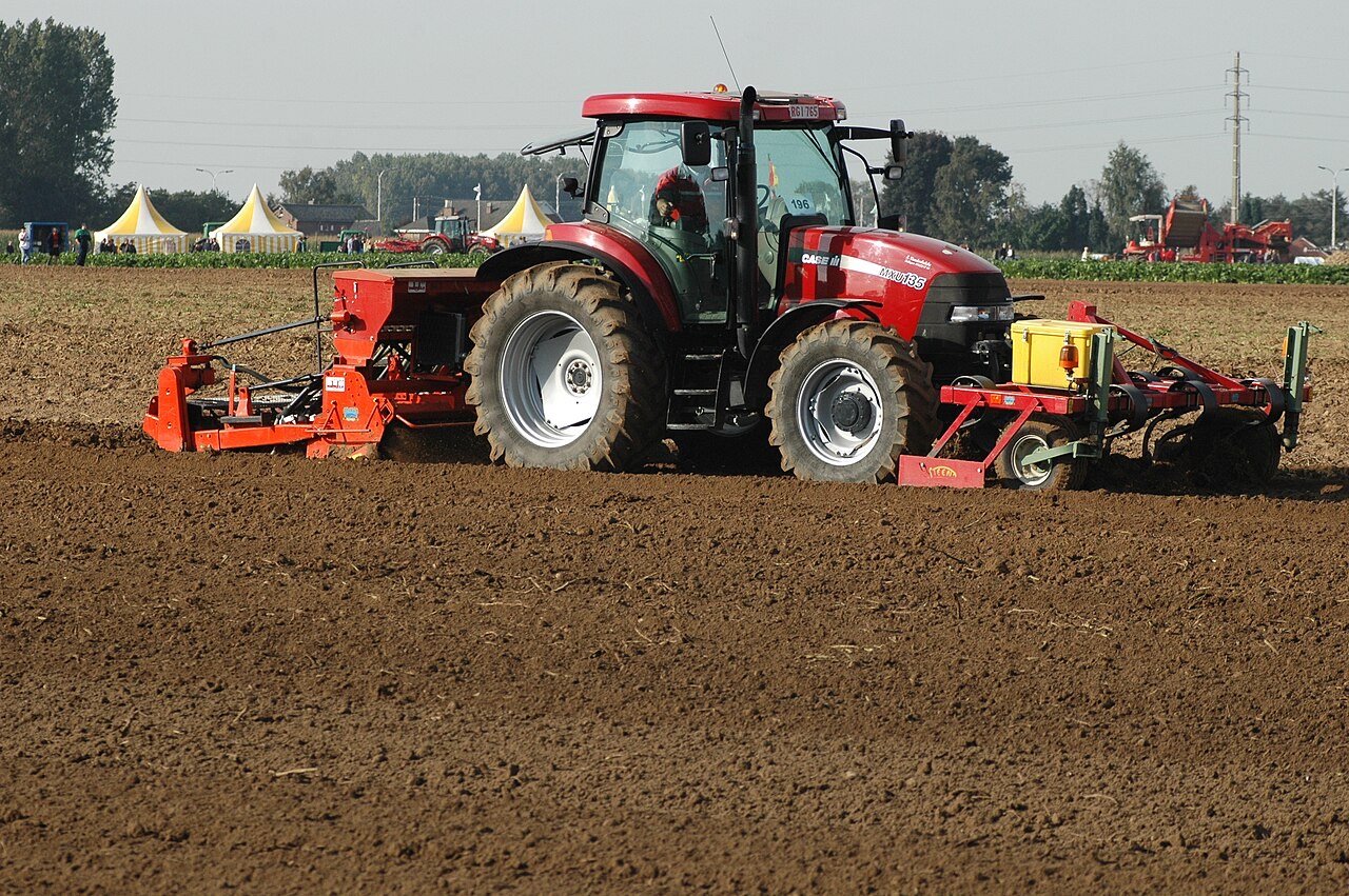 Red tractor pulling a seed drill across tilled soil