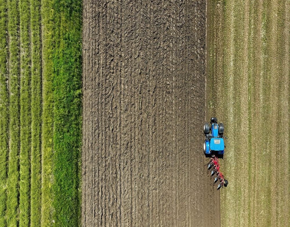Blue tractor ploughing farmland, aerial view