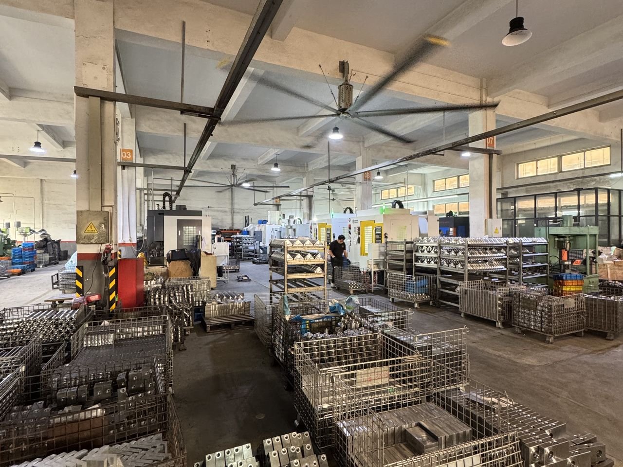 Production workshop aisle with finished machined components organized in steel baskets